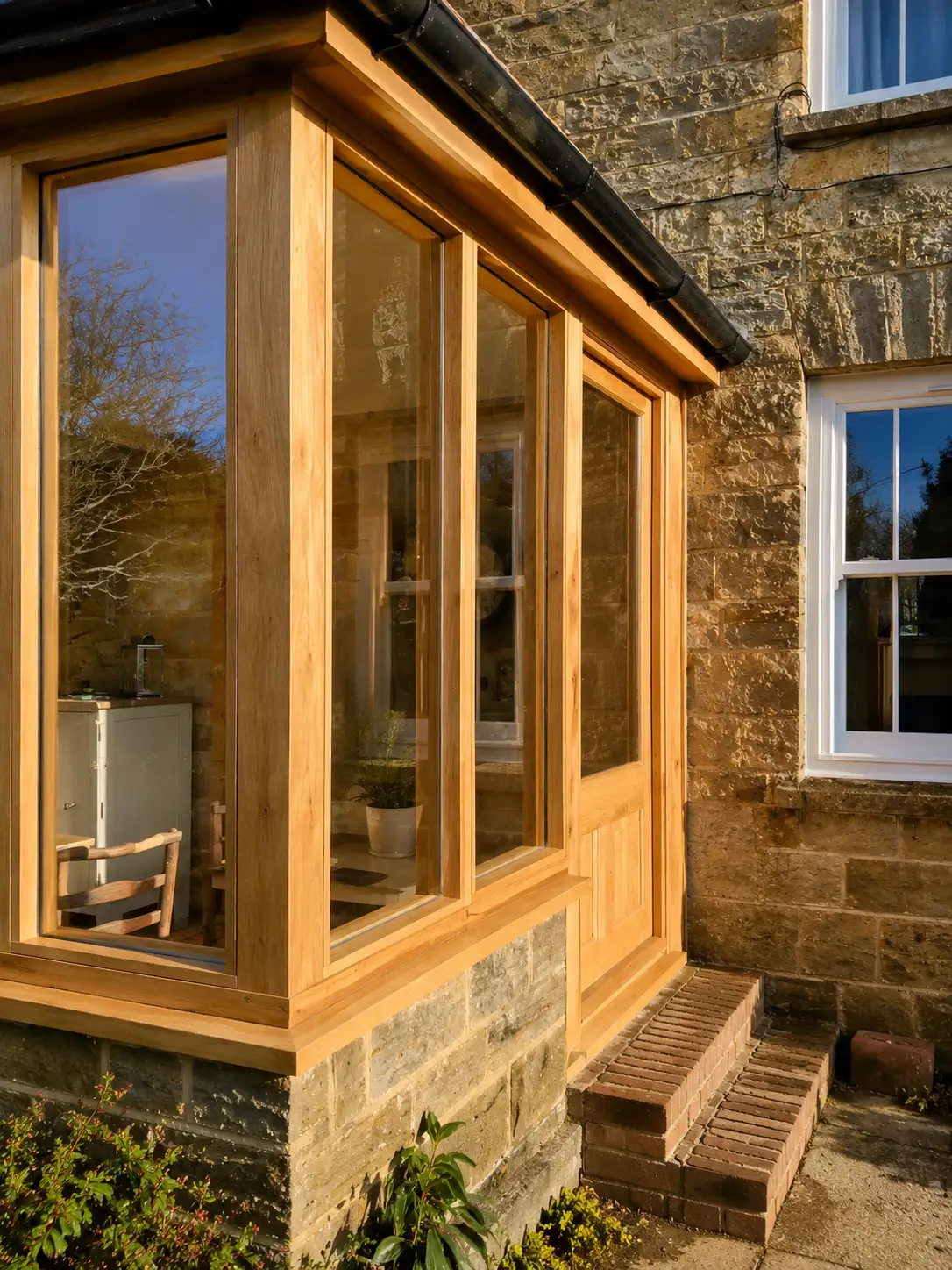 Close-up of an oak-framed glazed garden room extension against a Sussex stone cottage wall