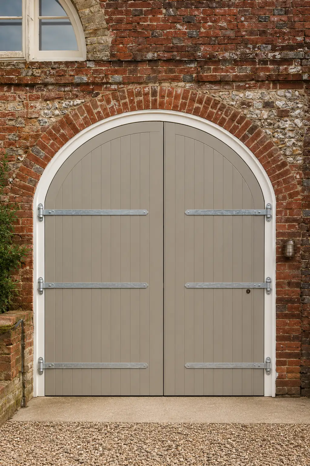 Pair of arched painted timber carriage doors with galvanised strap hinges in a brick archway