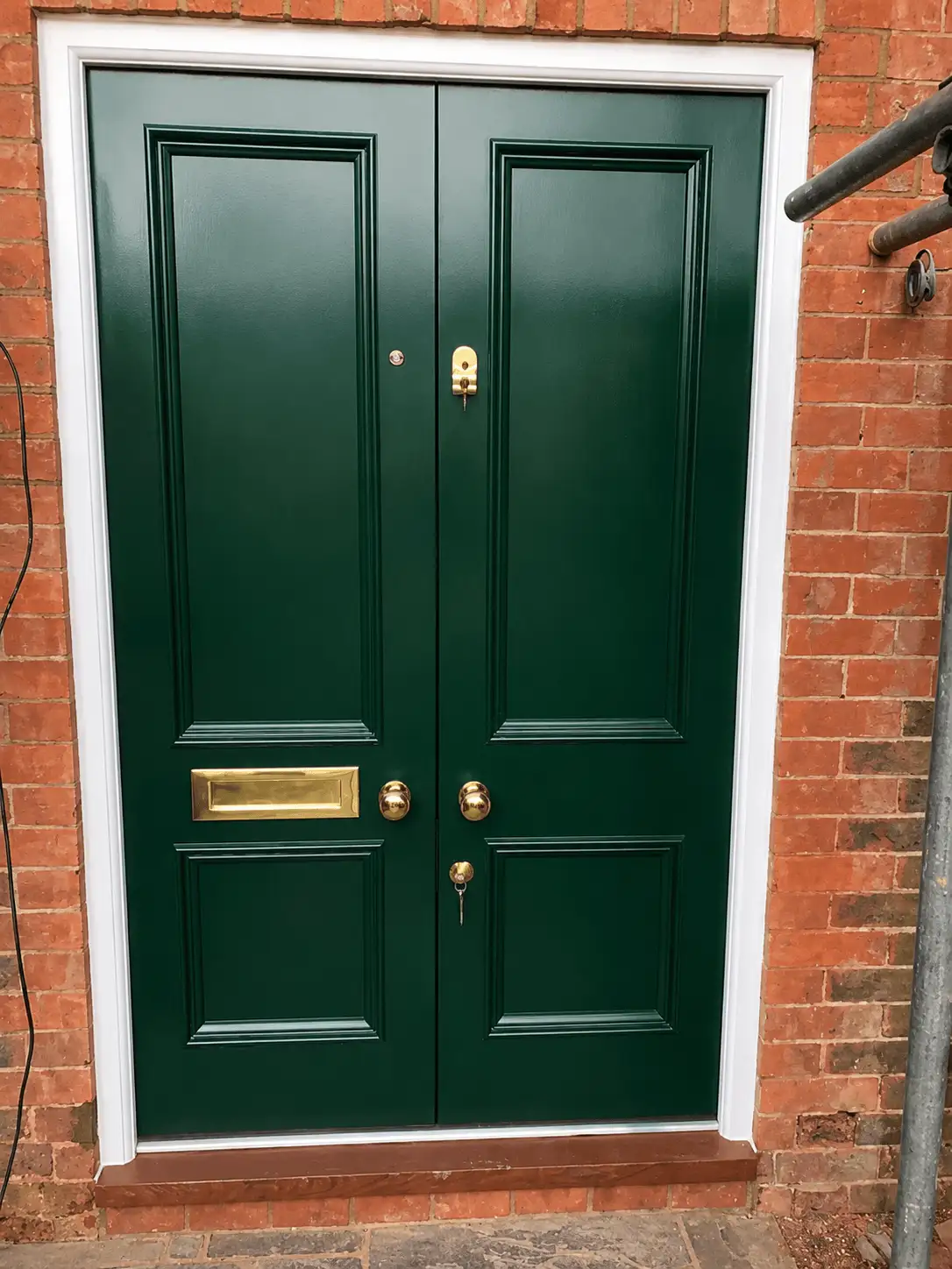 Dark green painted double front doors with raised-and-fielded panels and polished brass furniture, in a white-painted brick surround