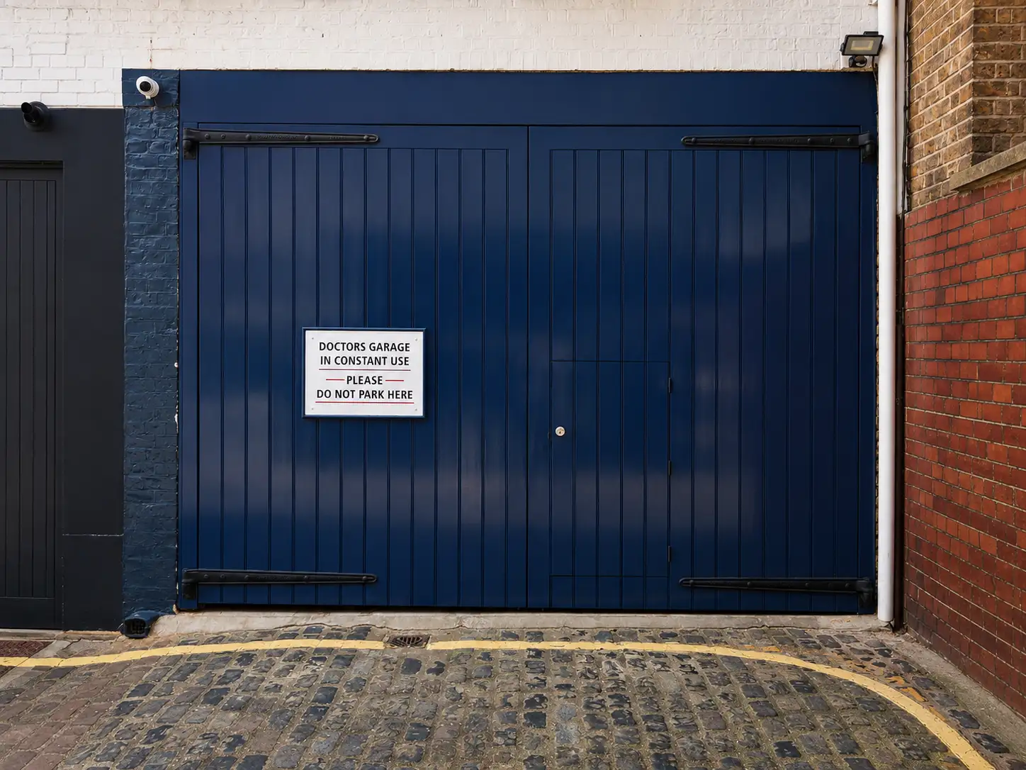 Pair of large navy-painted timber garage doors with galvanised strap hinges on a mews