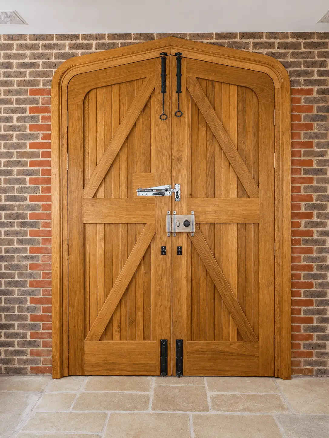 Oak arched ledged-and-braced double doors with black ring-pull ironmongery, set in a brick opening