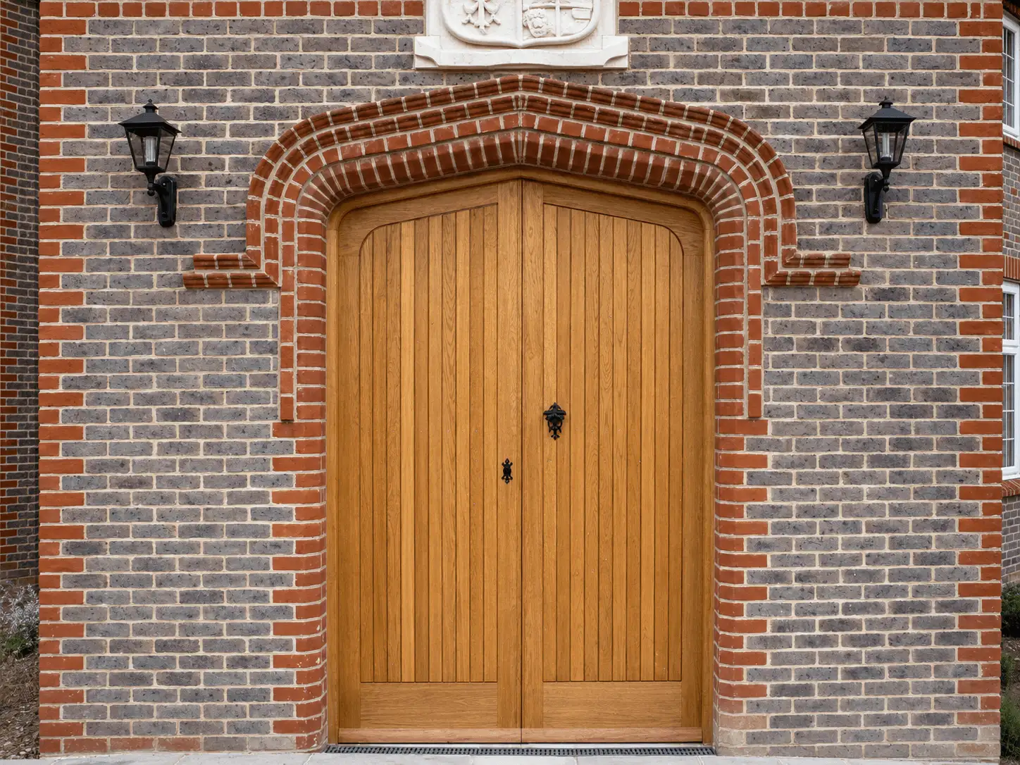 Oak arched double doors with vertical boarding, set in a decorative brick archway with coach lamps