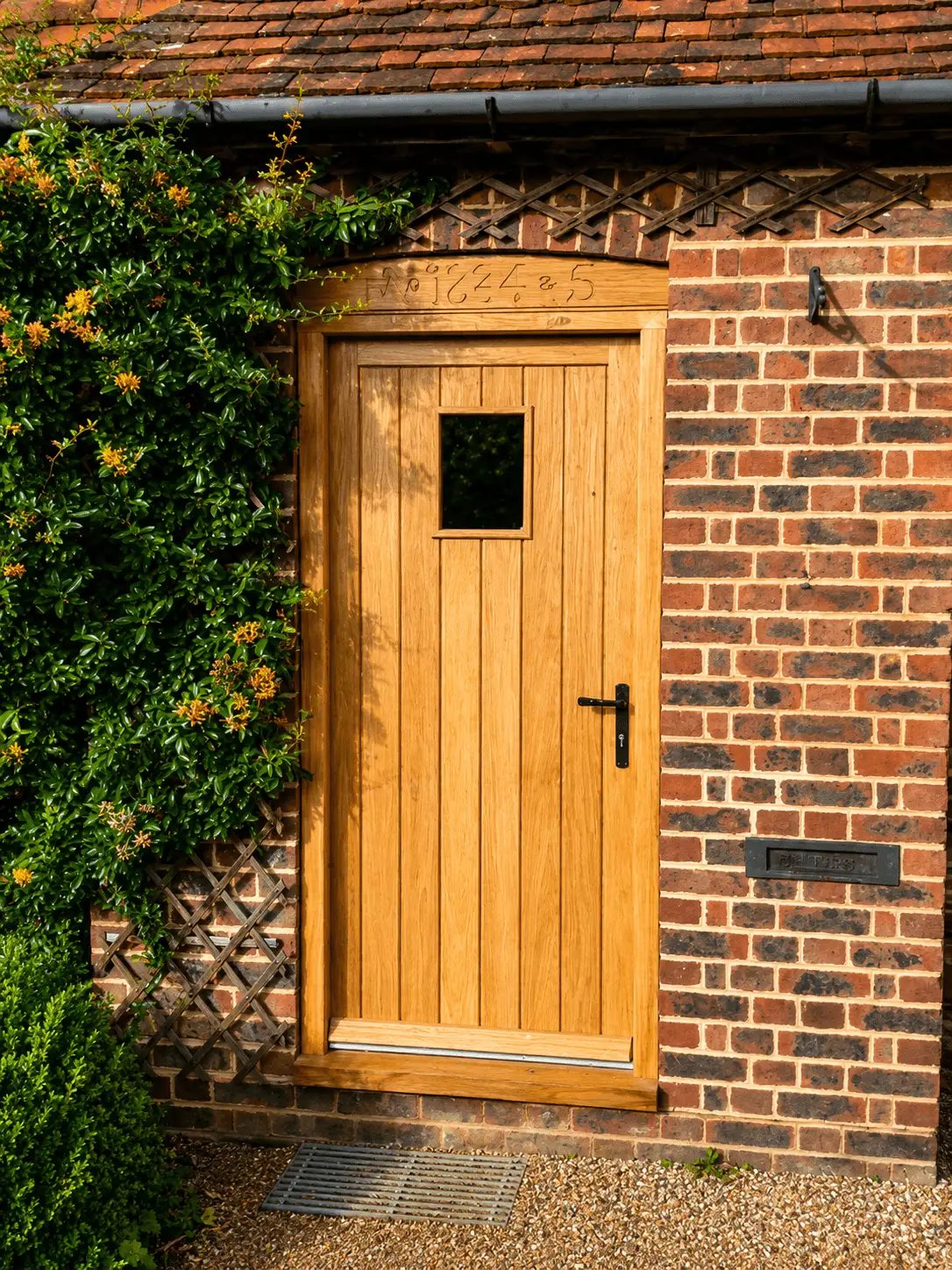 Oak boarded door with a small glazed light, under a dated brick lintel with climbing foliage