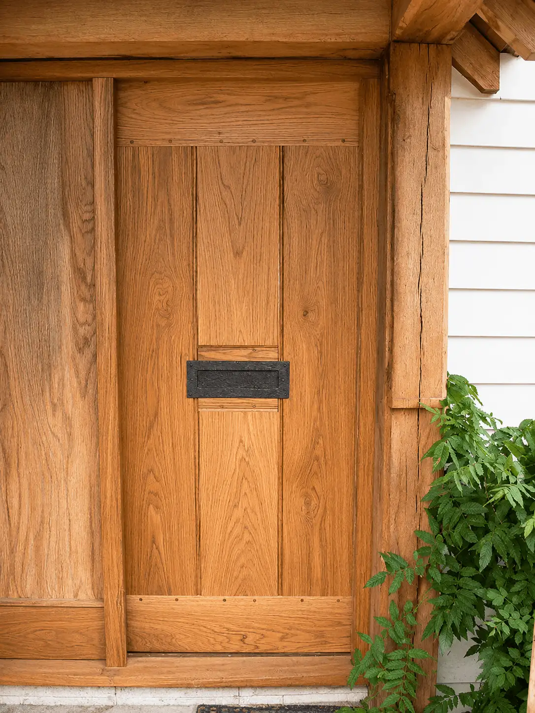 Oak boarded door with a black letterplate, set under an oak porch beside white weatherboarding