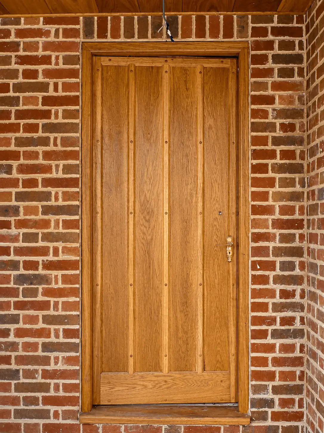 Oak boarded-and-studded door with brass furniture, set in a red-brick surround