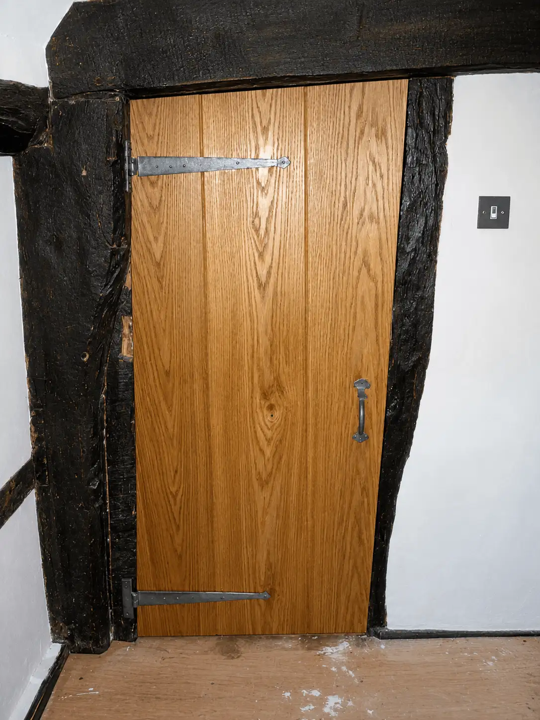Oak boarded door with galvanised strap hinges, fitted into a blackened oak timber-framed opening
