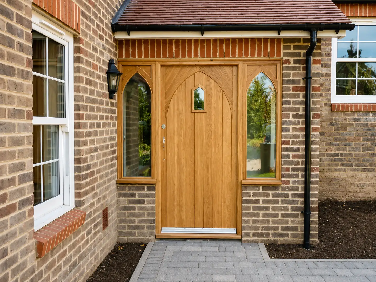 Hand-built oak front door with Gothic-arched glazed sidelights, set in a brick porch