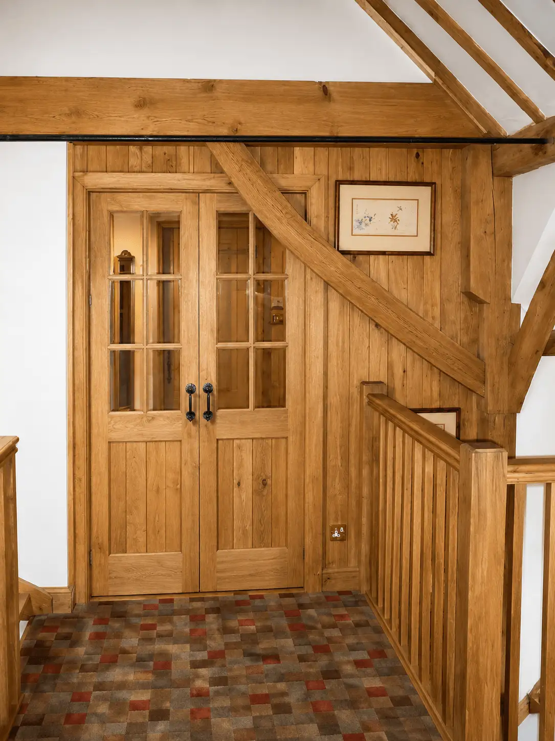 Oak internal double doors with six-pane glazed upper panels, set beneath a curved oak beam by an oak staircase
