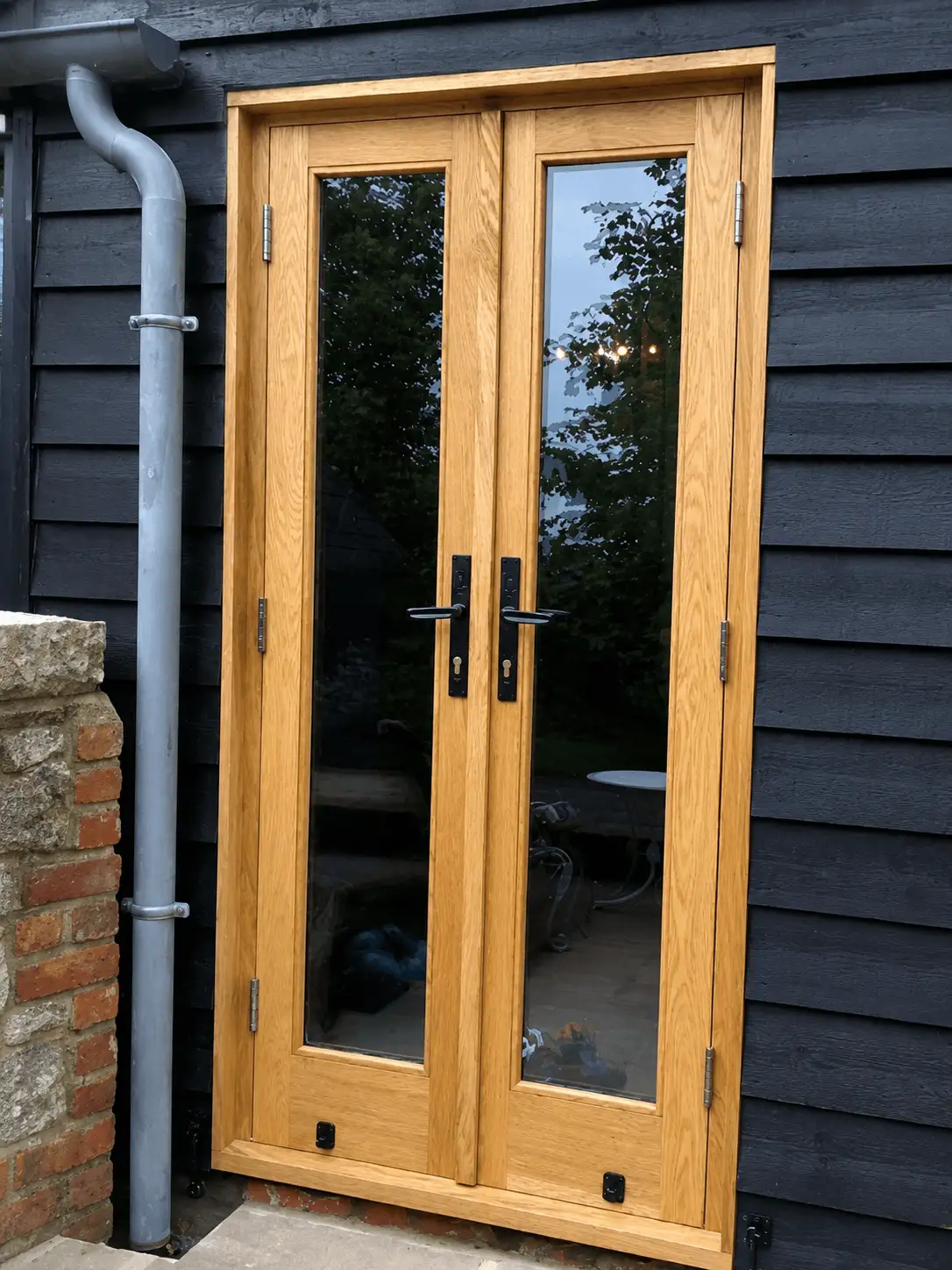Oak fully-glazed French doors with black ironmongery, set into black weatherboarding on a barn