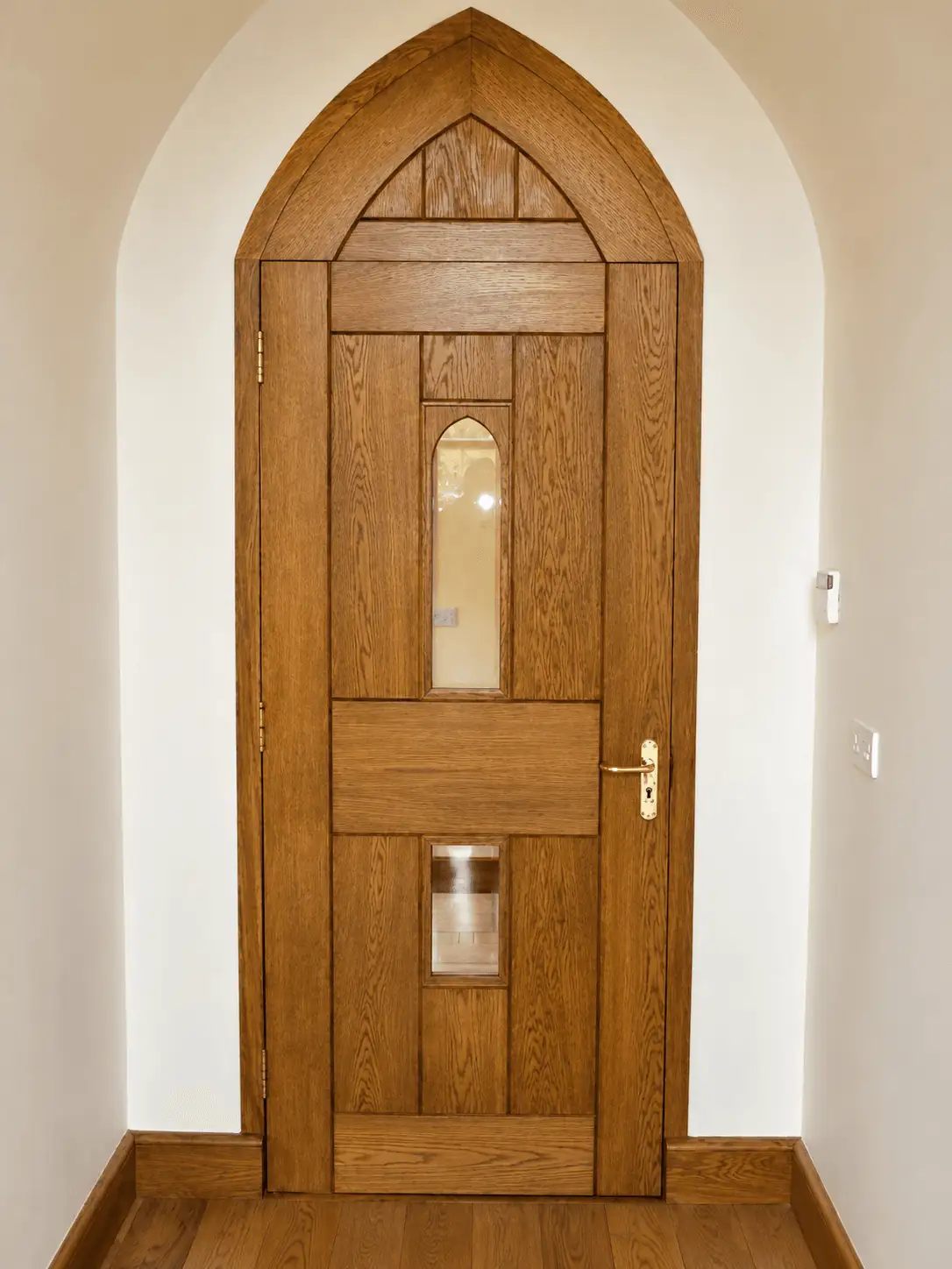 Oak Gothic-arched internal door with slim glazed lights, set in a plastered arched opening
