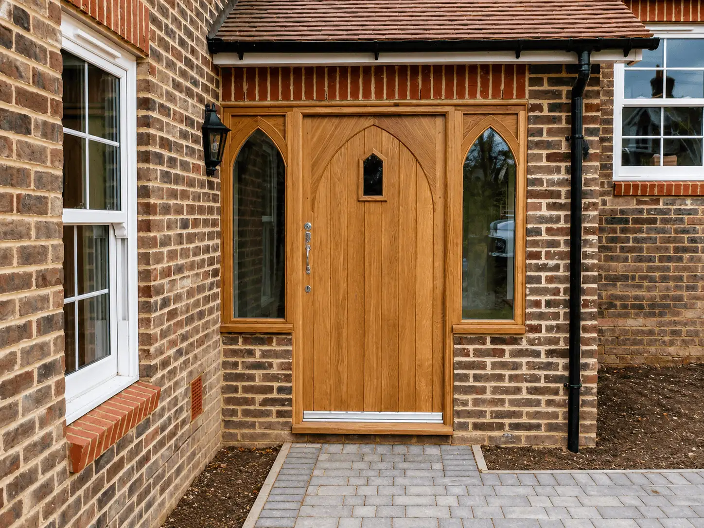Hand-built oak Gothic-arched front door with a small leaded light, flanked by arched glazed side panels in a brick surround