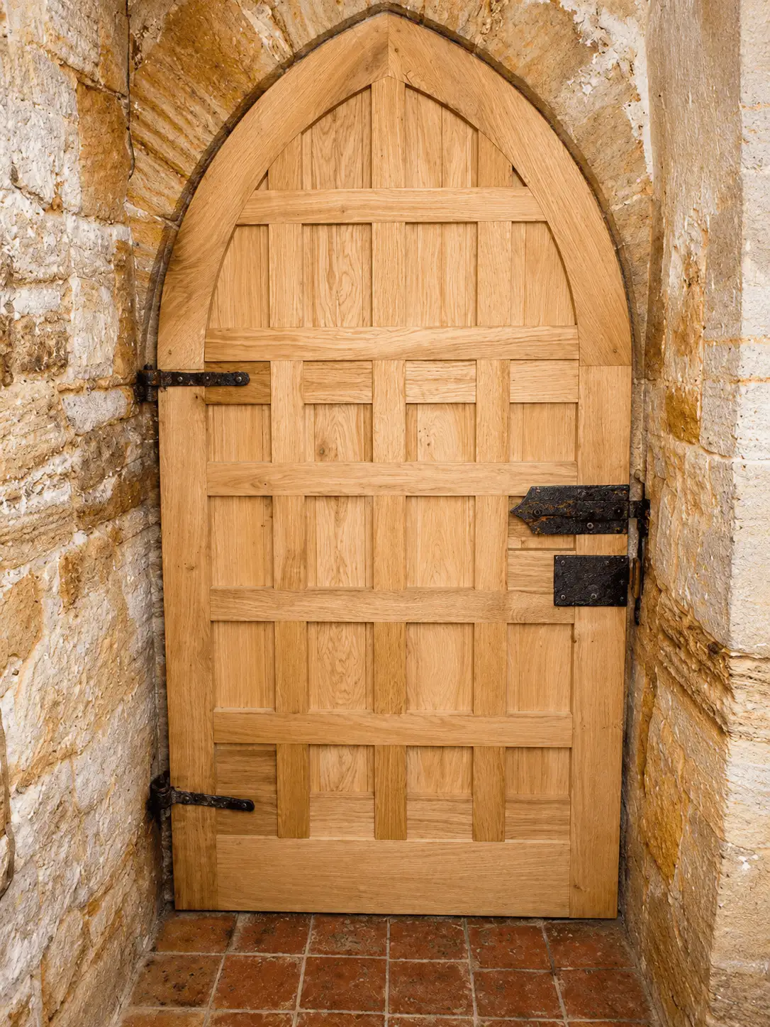 Oak Gothic-arched multi-panel door with strap hinges, set in a stone arched opening