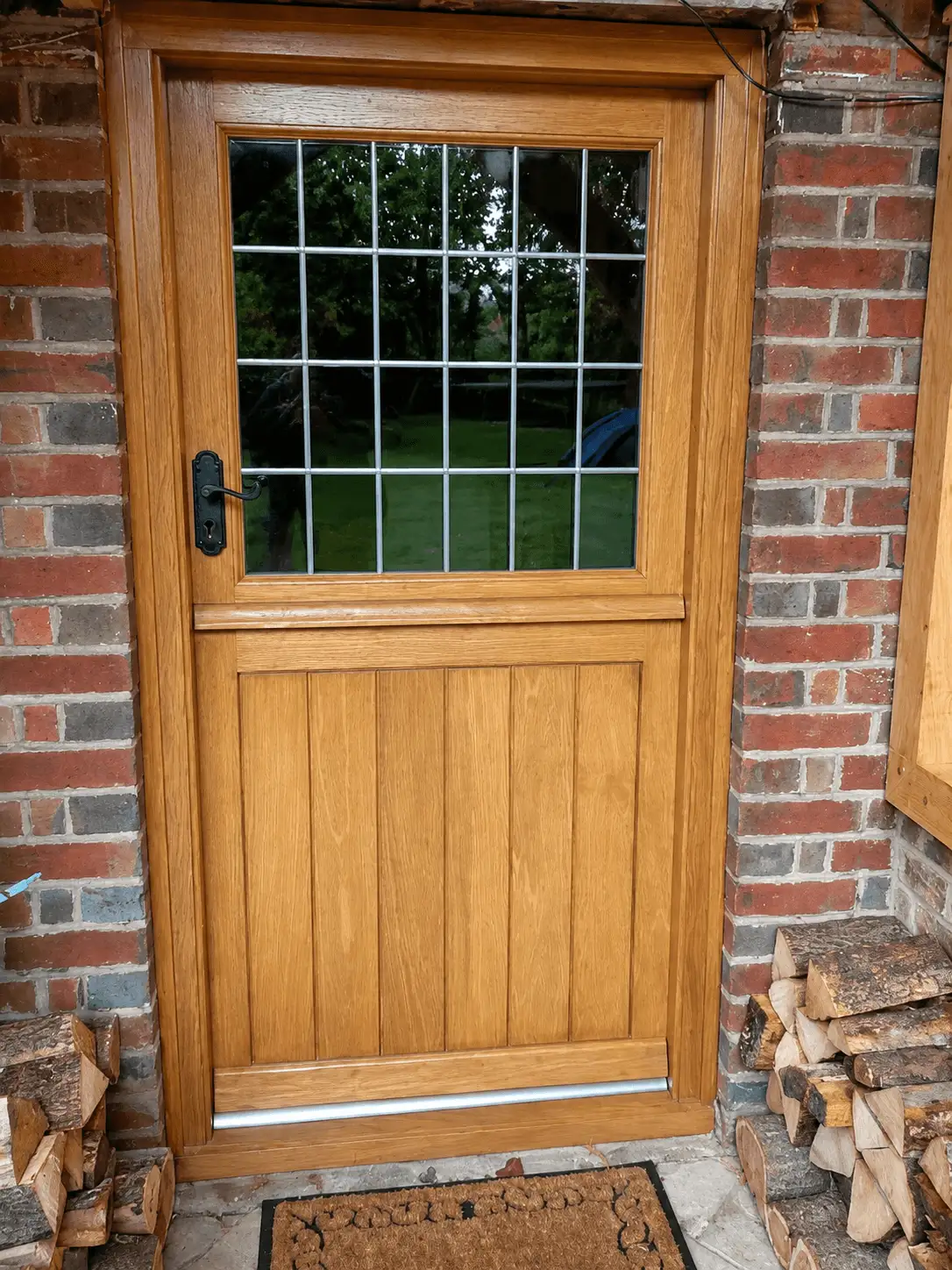 Oak stable door with a leaded glazed top and a boarded base, black ironmongery, in a brick opening