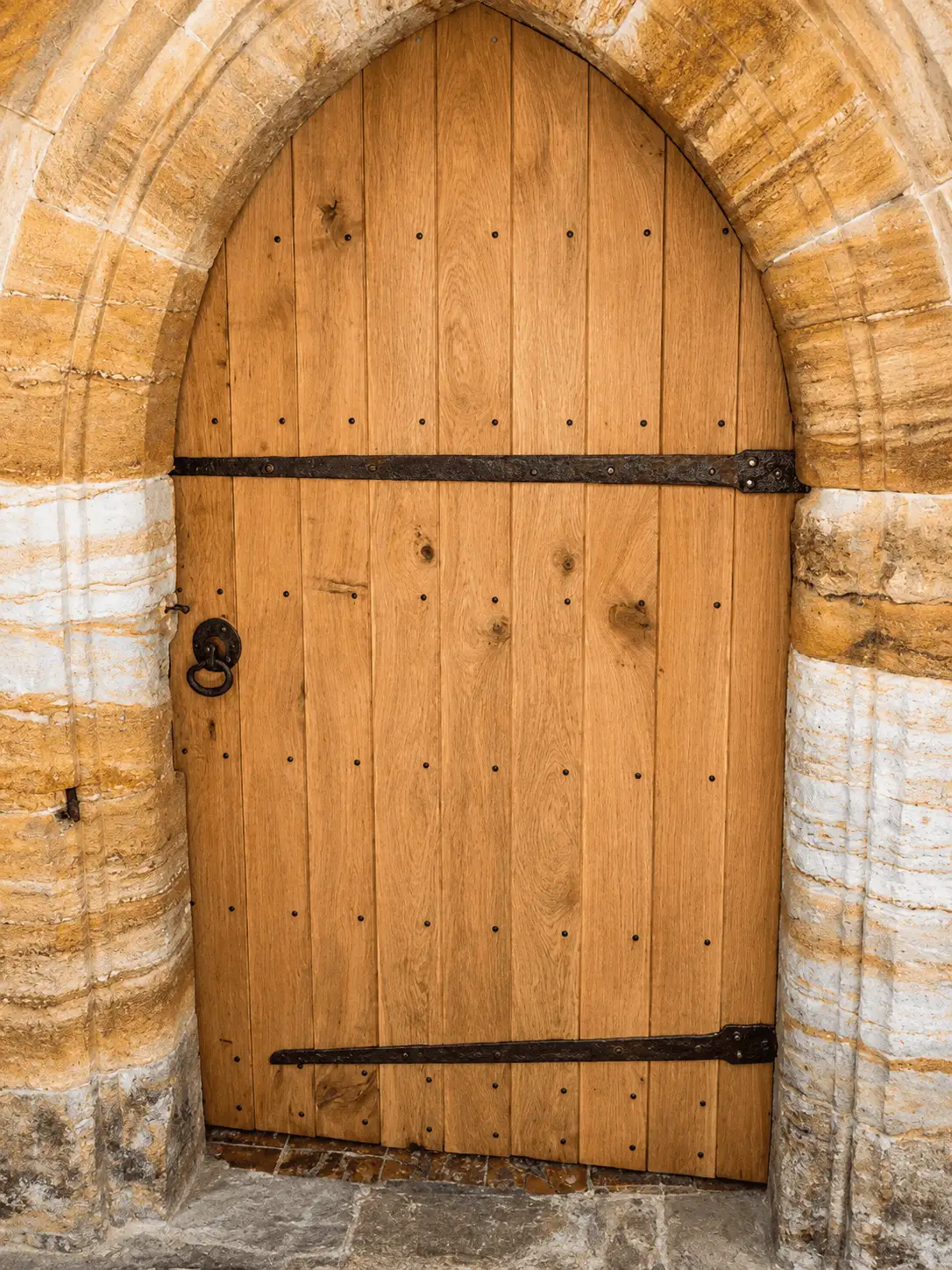Oak boarded-and-studded door with an iron ring latch, set in a stone Gothic-arched opening