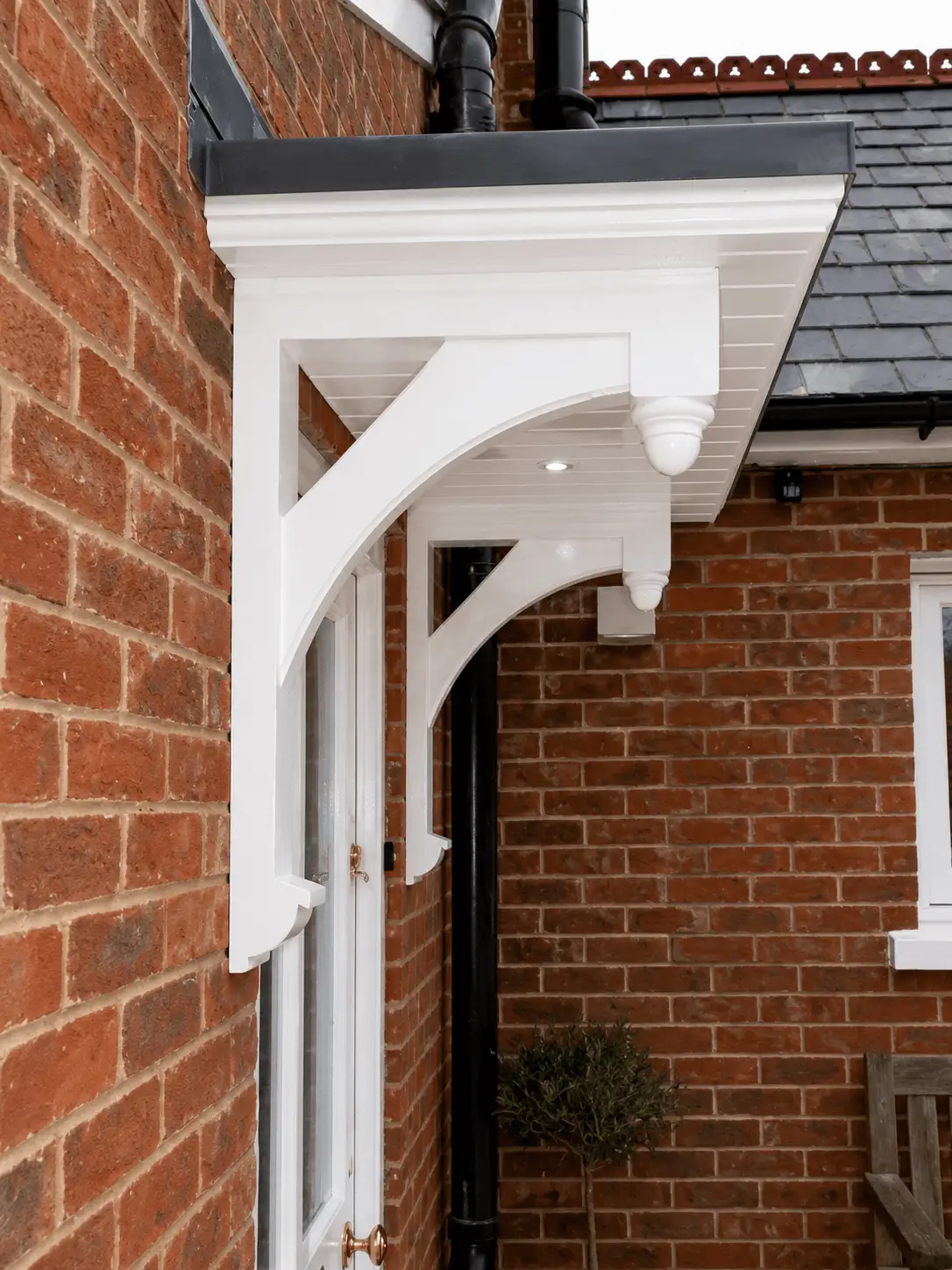 White painted timber entrance canopy on curved gallows brackets, fitted over a doorway in a brick wall