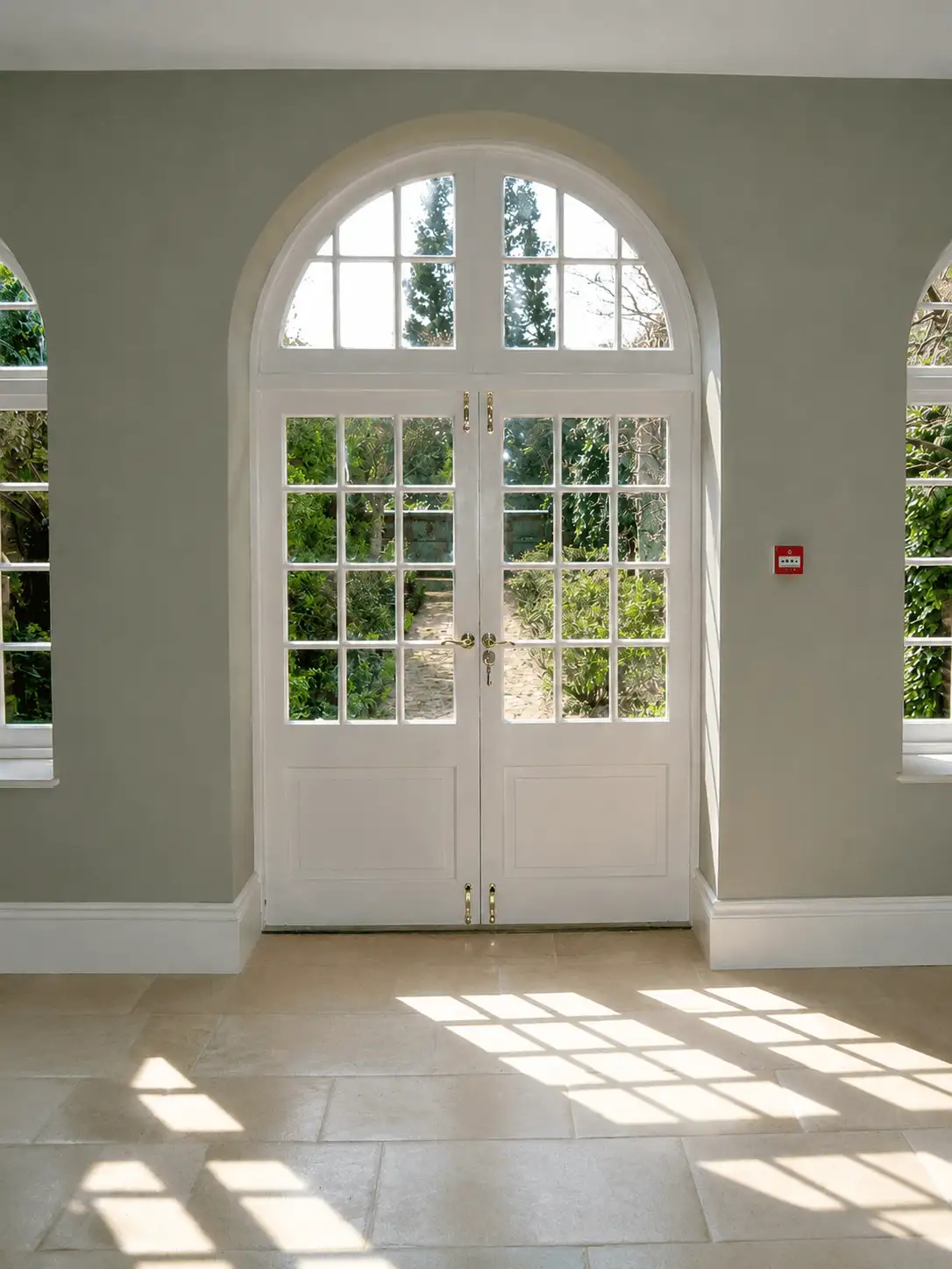White painted arched French doors with Georgian glazing bars and a fanlight, flanked by arched windows in a garden room
