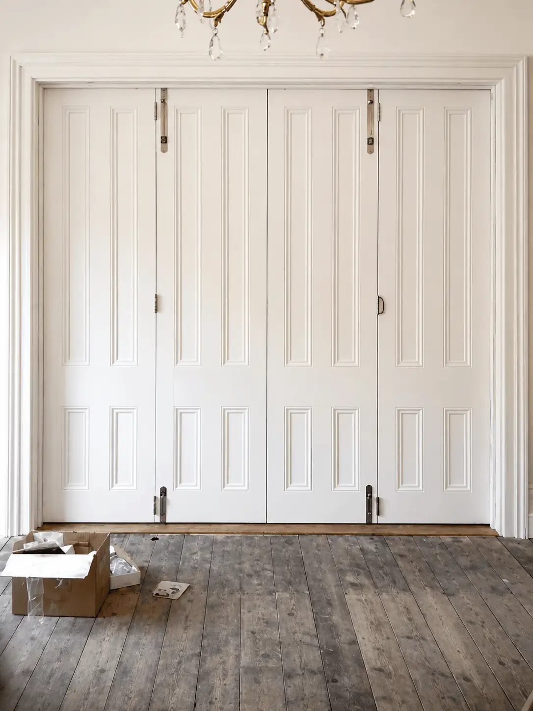 White painted folding internal doors with raised-and-fielded panels and polished hinges in a period room
