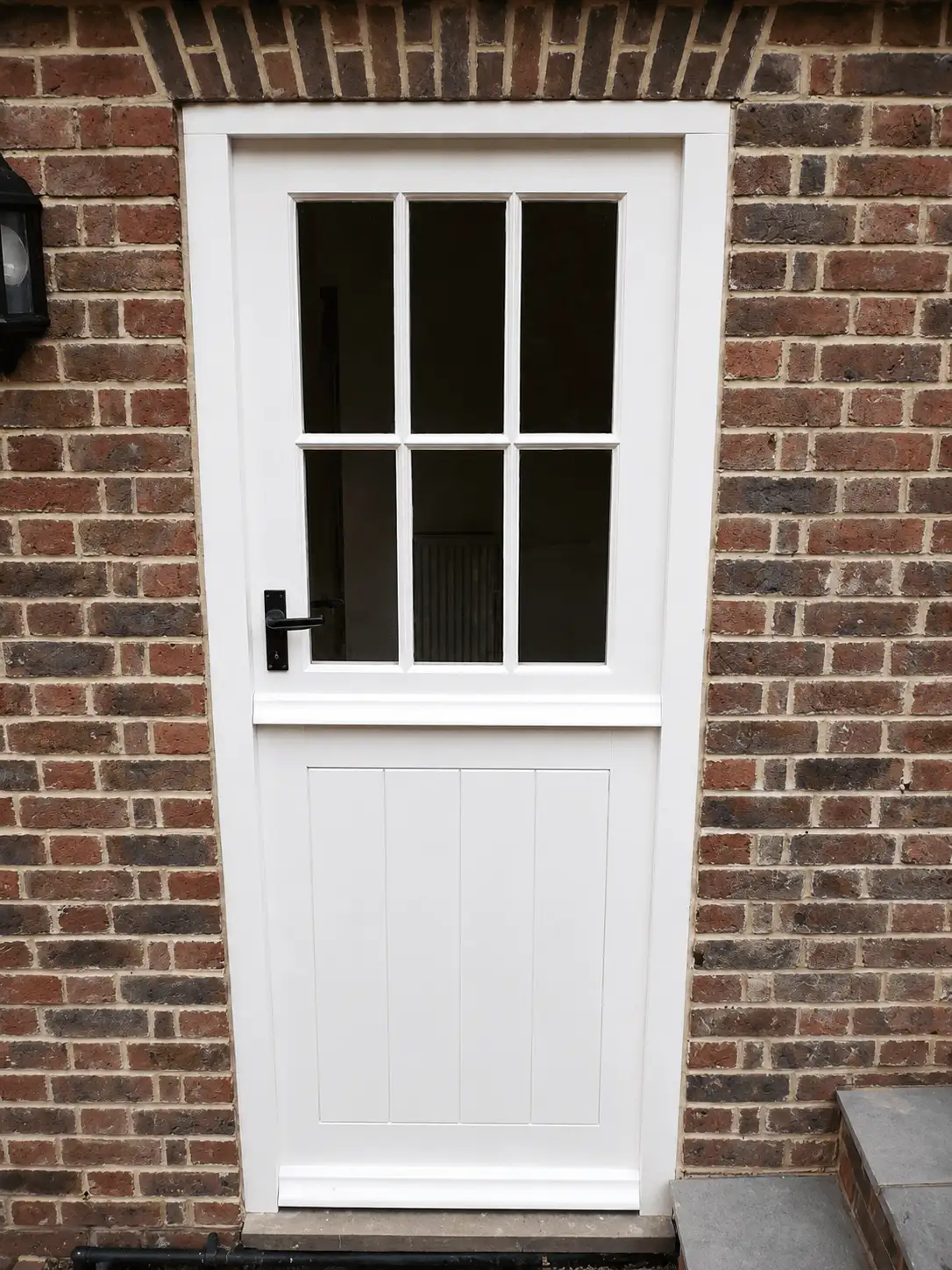 White painted stable door with a six-pane glazed top and a boarded base, black ironmongery, in a brick opening