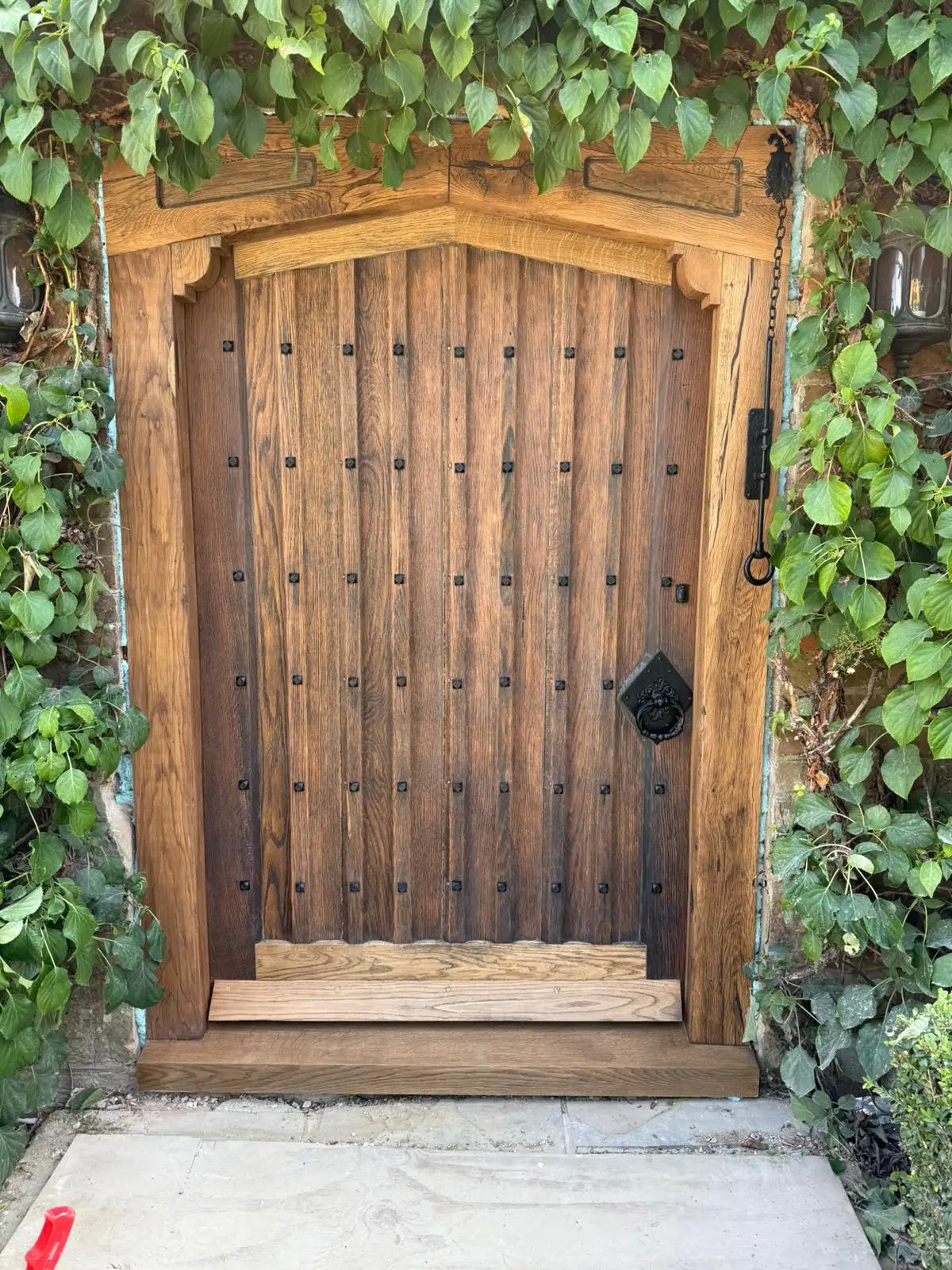 Restored studded oak door, sanded and finished, rehung in a stone reveal with greenery either side