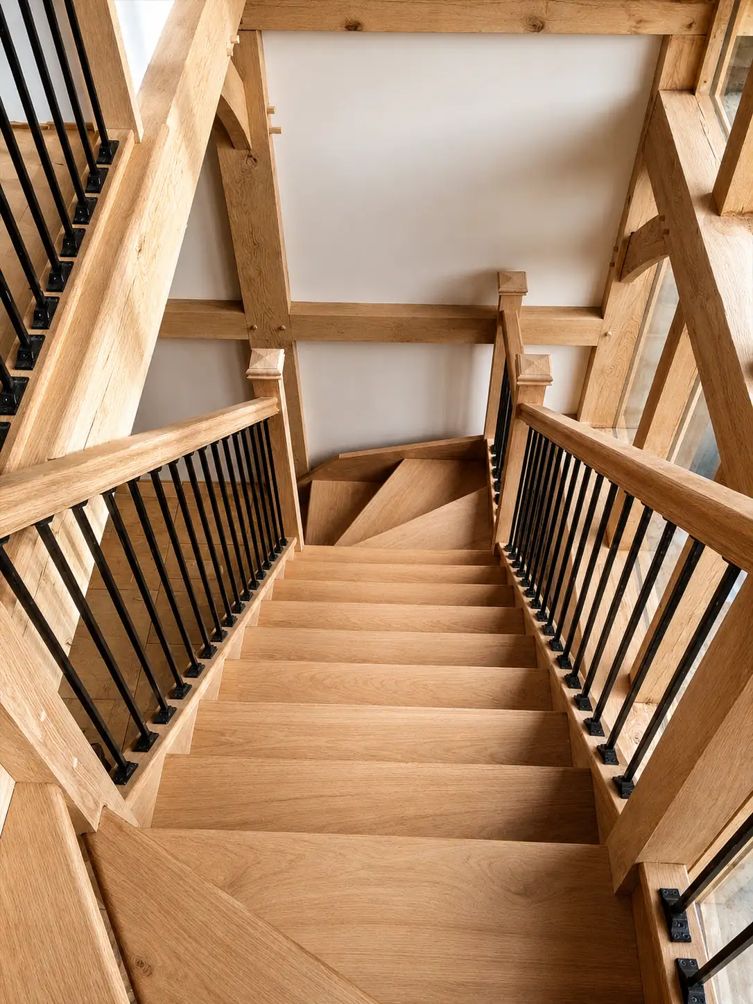 Oak staircase with black metal spindles winding through an oak-frame house, looking down