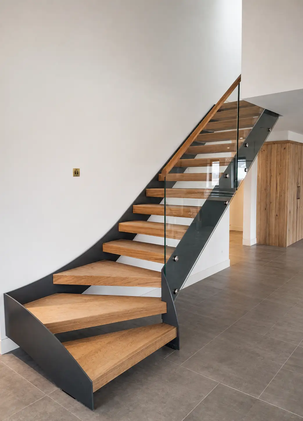 Contemporary oak open-tread staircase with a dark steel stringer and frameless glass balustrade