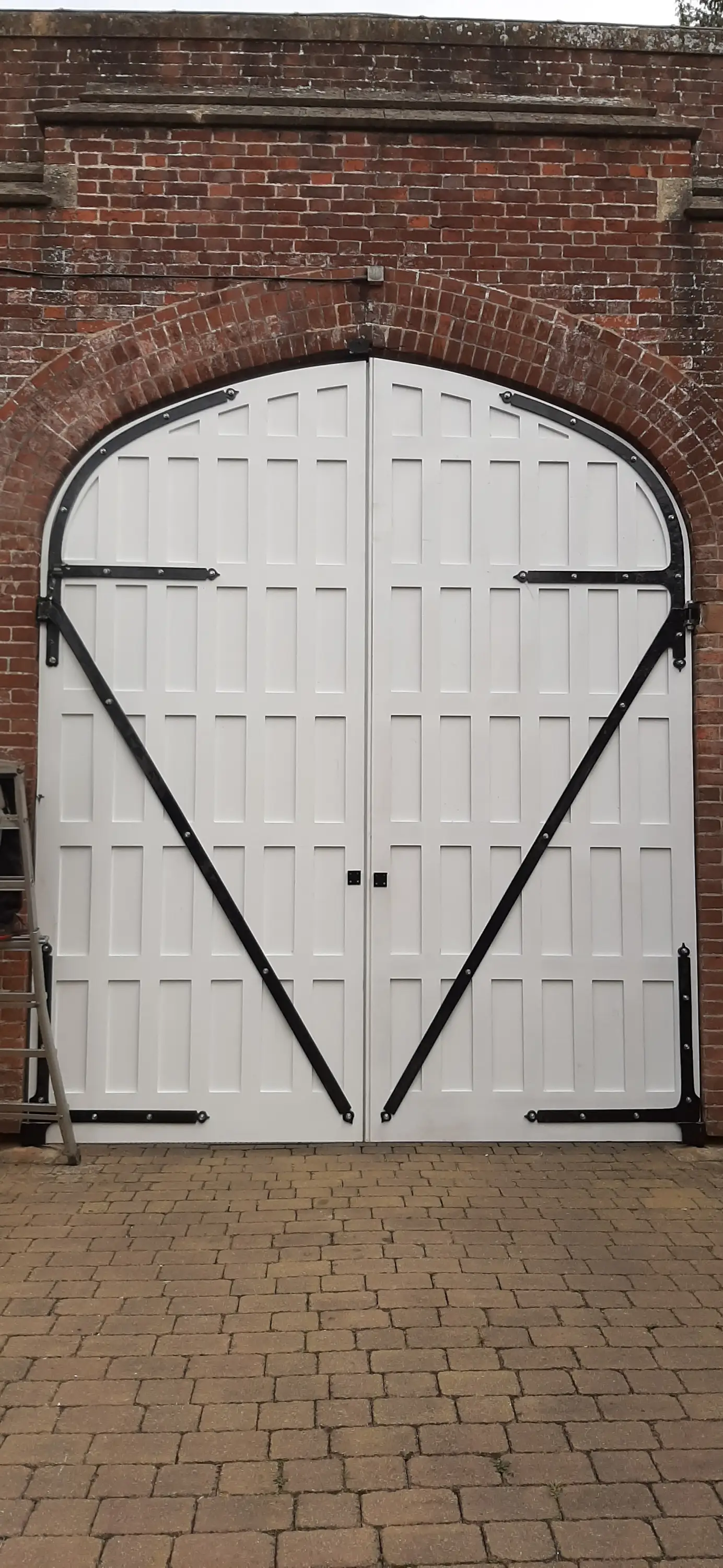 Hand-built arched double doors with black strap hinges in a red-brick archway