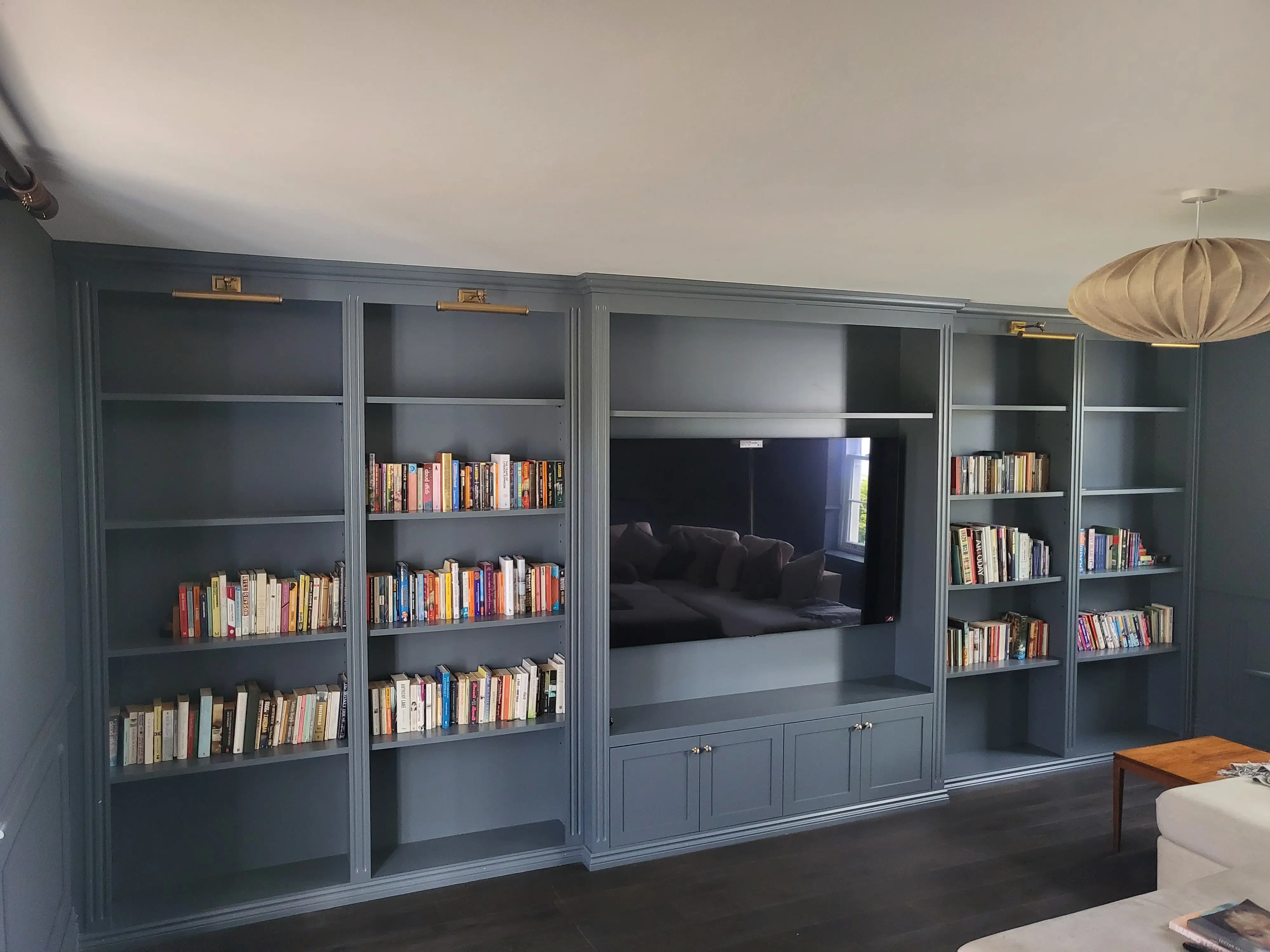 Bespoke slate-blue panelled media wall with bookcases and brass picture lights