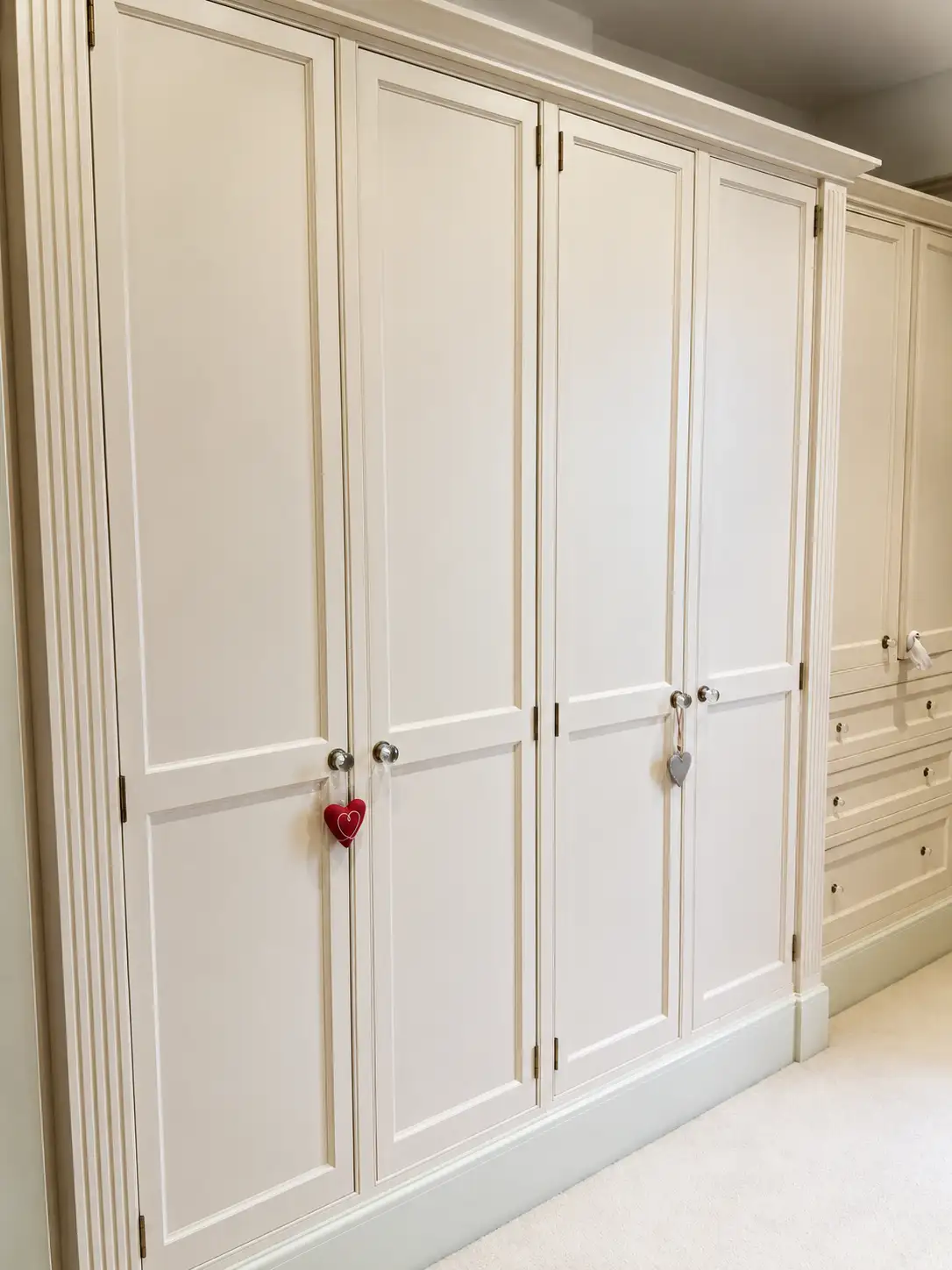 Cream classical fitted wardrobes with fluted pilasters, panelled doors and chrome knobs in a dressing area