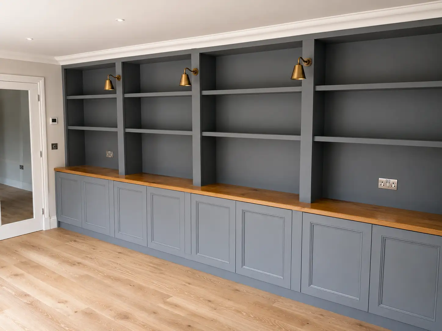 Floor-to-ceiling slate-grey fitted shelving and dresser with an oak worktop, brass picture lights and panelled cupboard bases