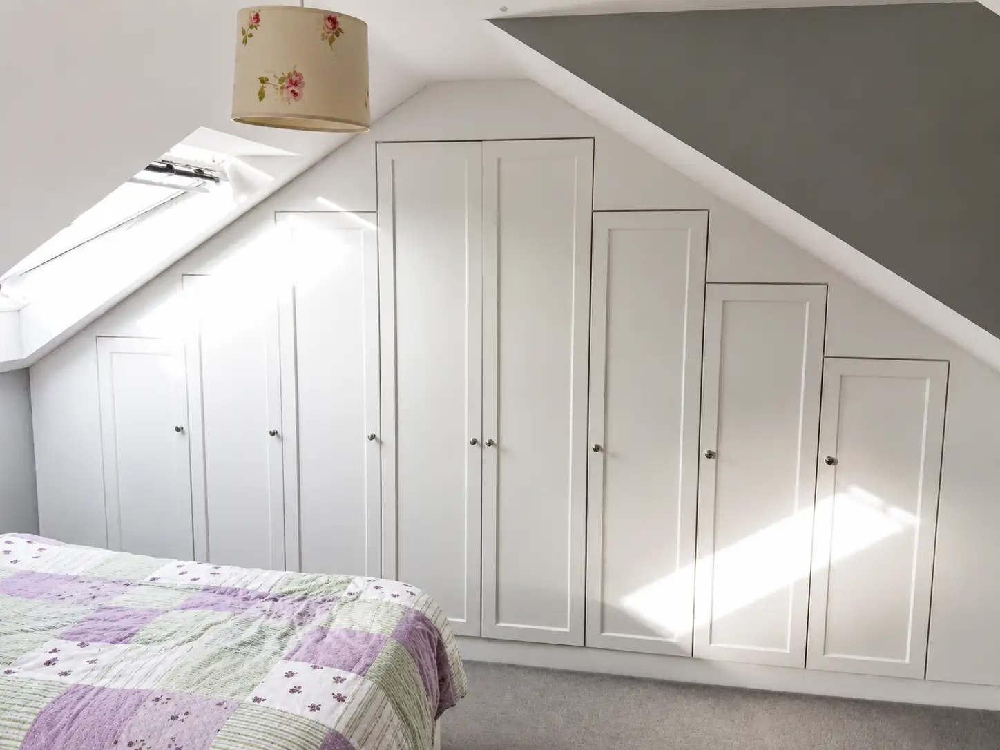 White shaker fitted wardrobes built into a loft bedroom, stepped to follow the sloped eaves