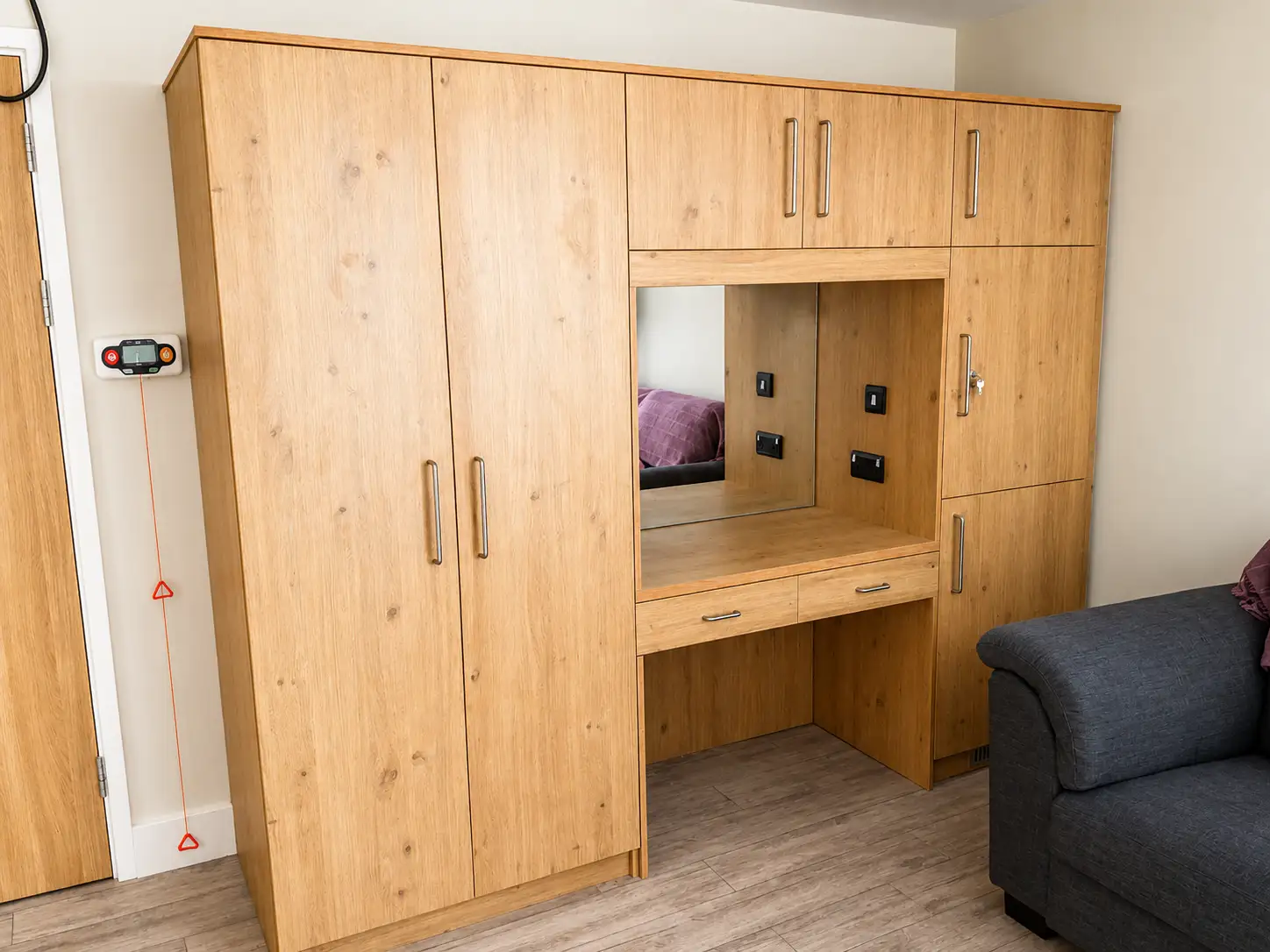 Oak-veneer fitted wardrobe run with an integrated mirrored dressing table and overhead cupboards