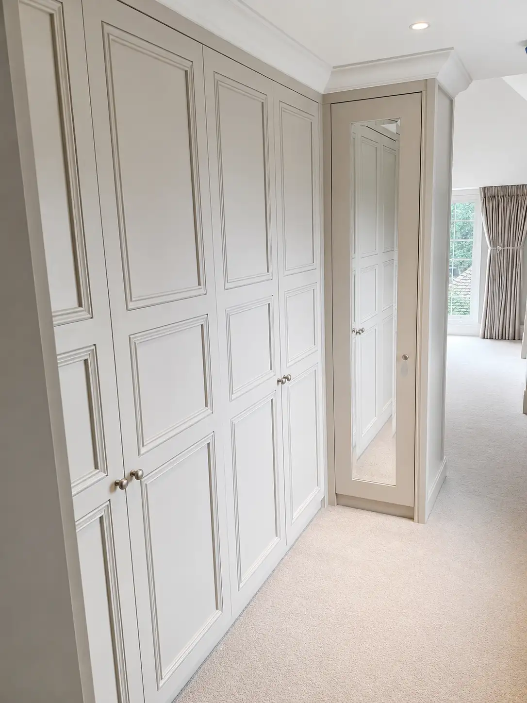 Floor-to-ceiling panelled fitted wardrobes in a dressing area with a full-length mirror cabinet