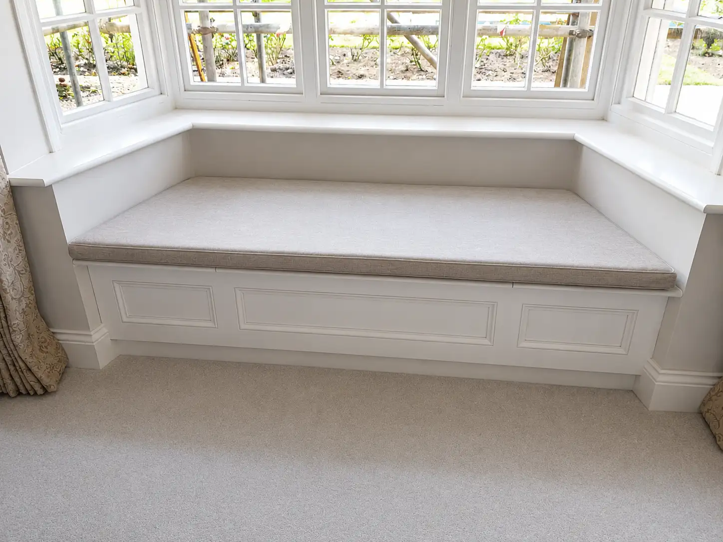 White panelled fitted window-seat bench built into a bay window with an upholstered cushion