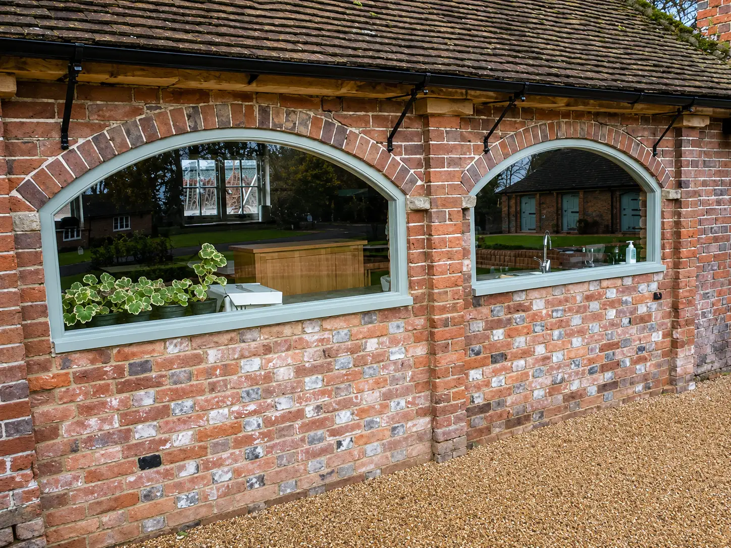 Two brick-arched fixed windows with sage-painted frames on a garden room outbuilding