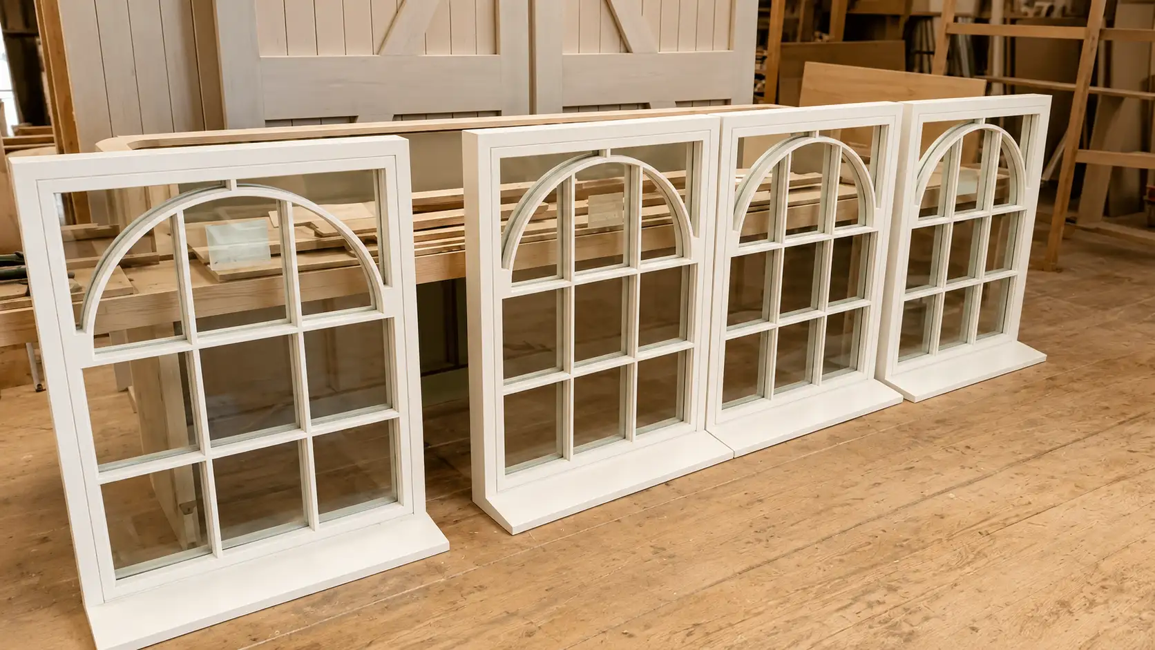 Four hand-built arched sash windows lined up in the Forest Joinery workshop, primed