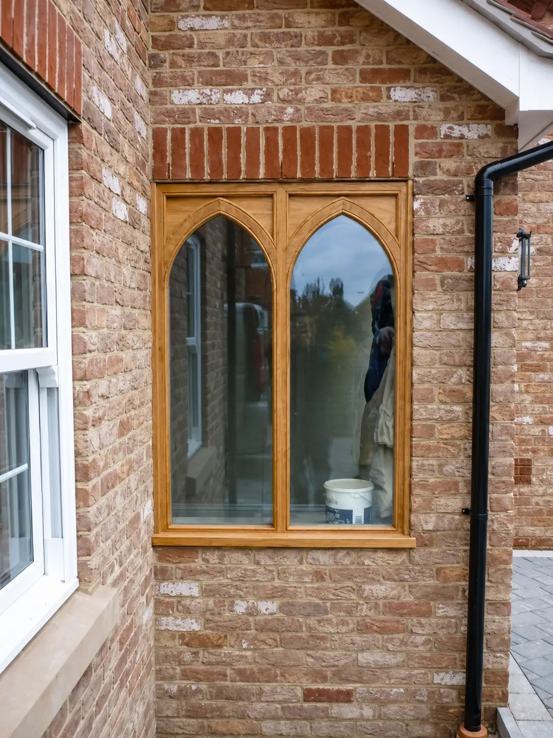 Twin Gothic pointed-arch oak casement window set in a red-brick wall with a brick arch head