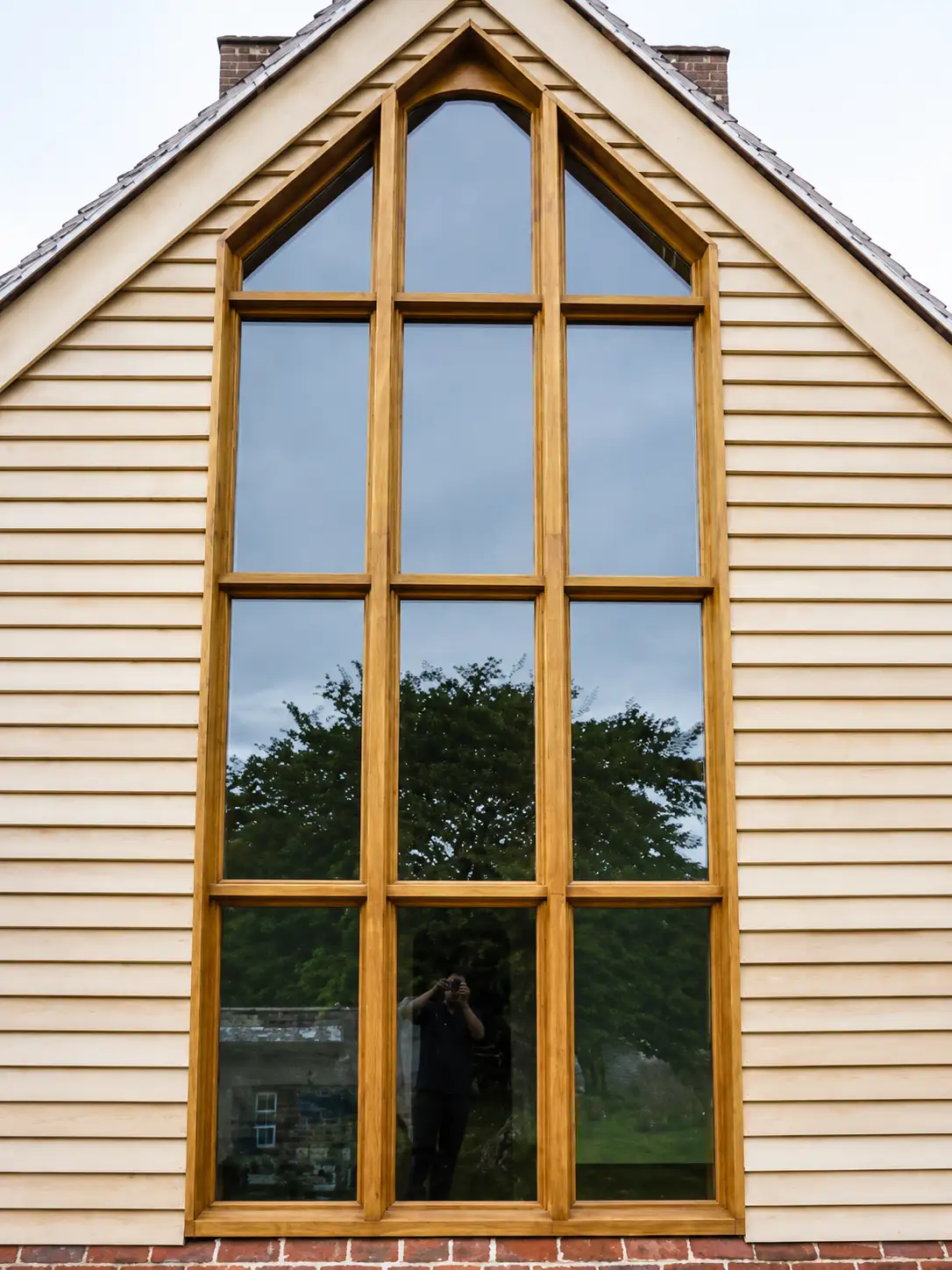 Full-height oak-framed multi-pane apex window in a cream weatherboard gable