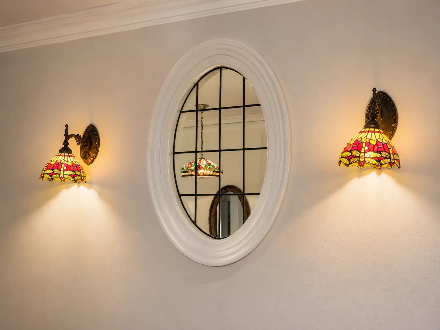 Oval leaded window with a moulded white frame between Tiffany wall lights