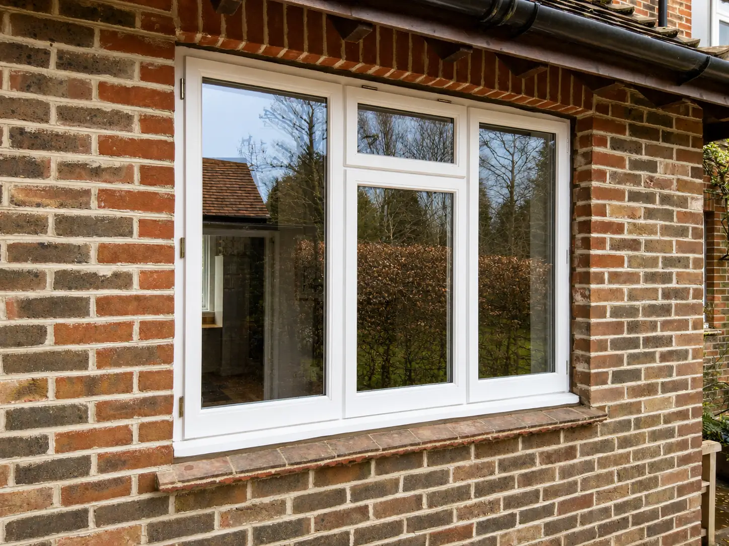 Three-light white casement window on a red-brick wall with tile sill detail