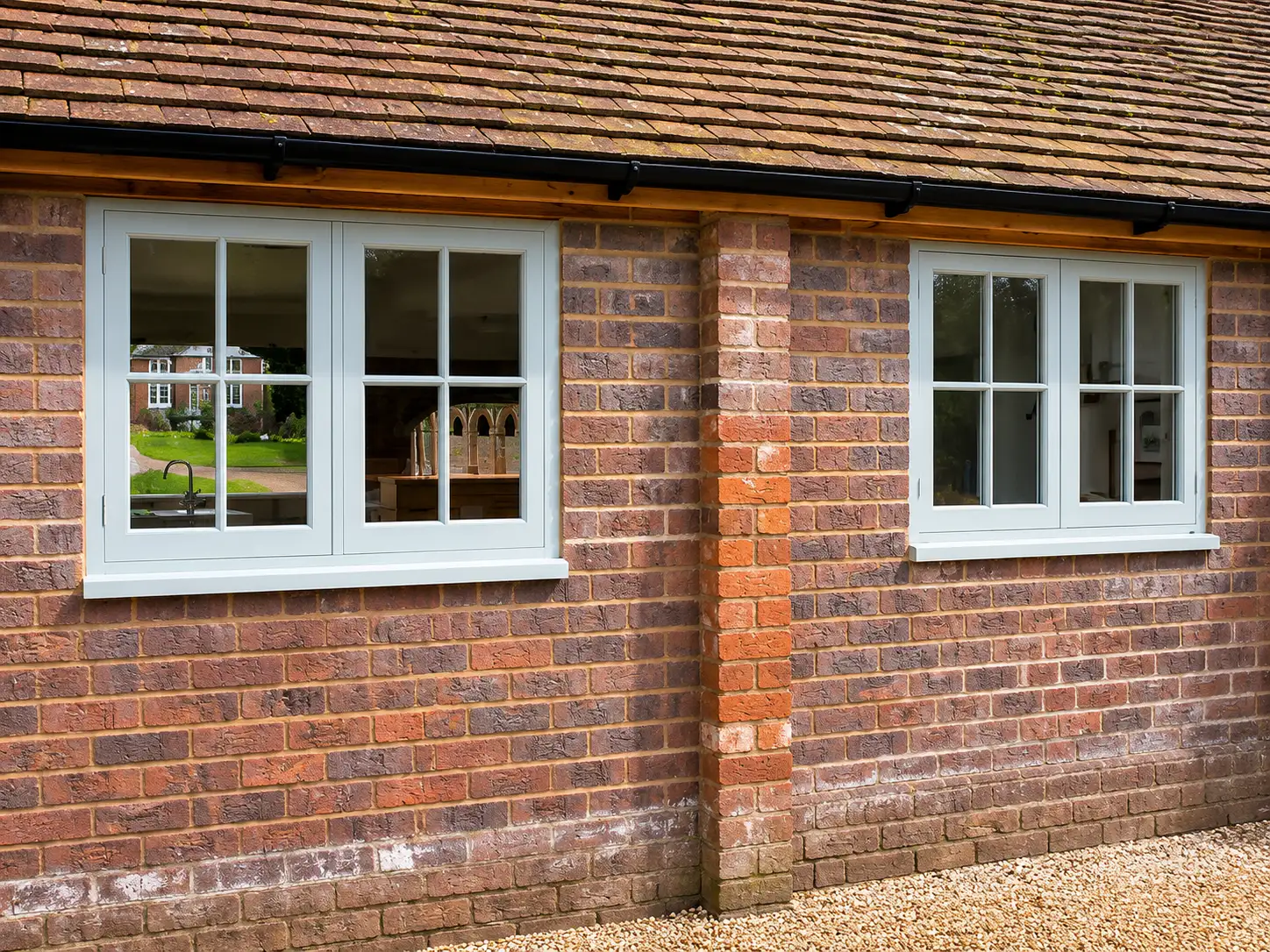 Sage-painted casement windows with Georgian glazing bars on a red-brick single-storey elevation