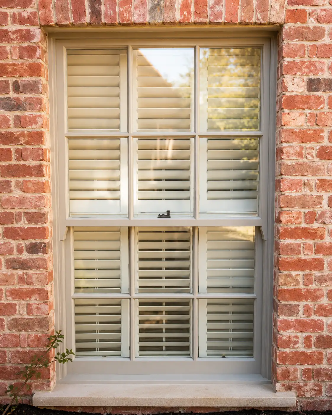 Traditional timber sliding sash window with internal shutters in a red-brick wall